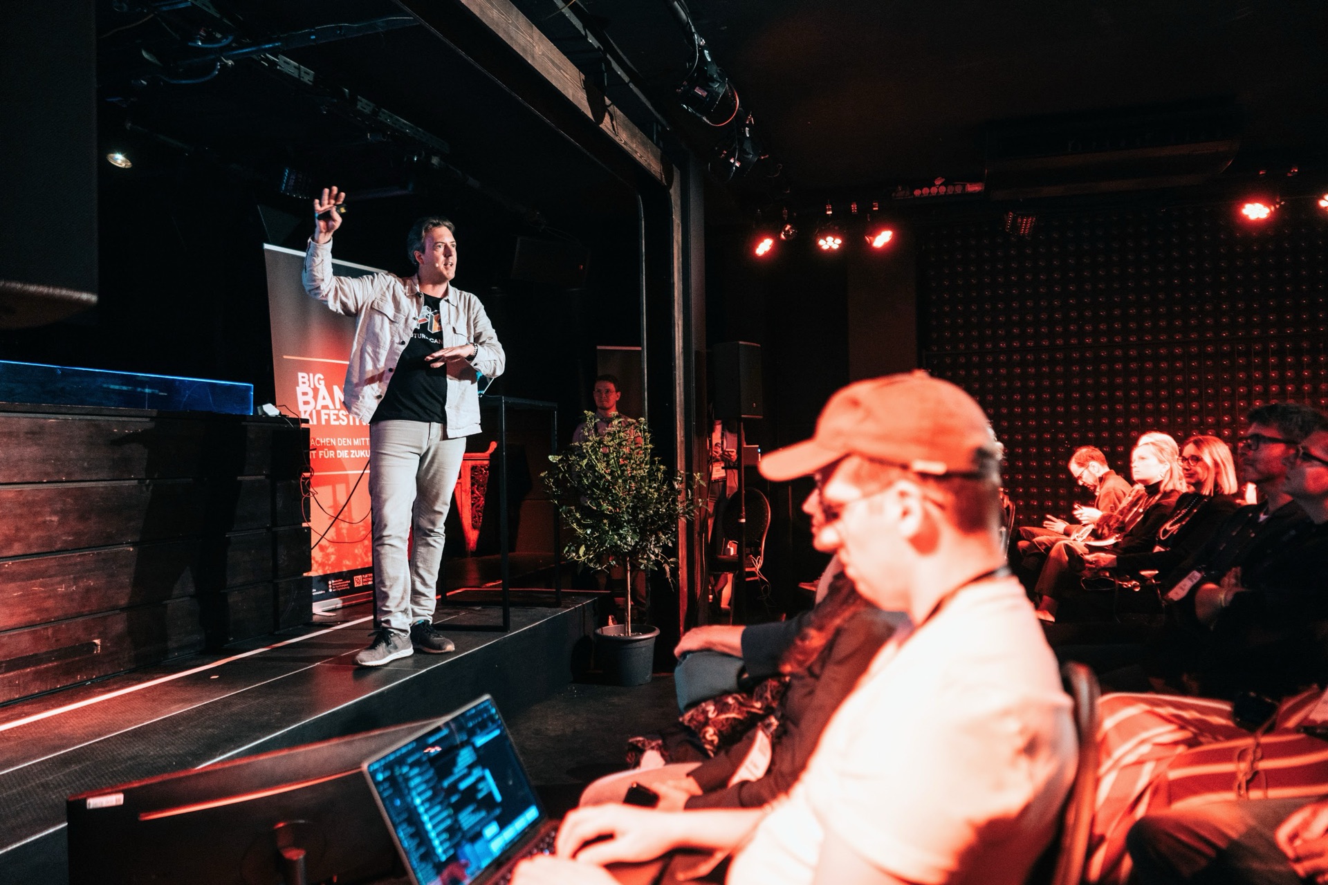 Roman Weishäupl on stage at Big Bang Festival – atmospheric stage lighting, participant with laptop in foreground