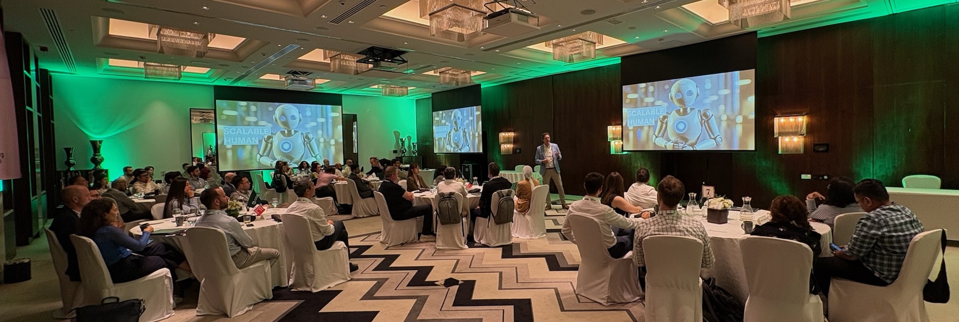 Roman Weishäupl hält die Keynote beim KI Bootcamp – großer Saal mit Teilnehmern an runden Tischen