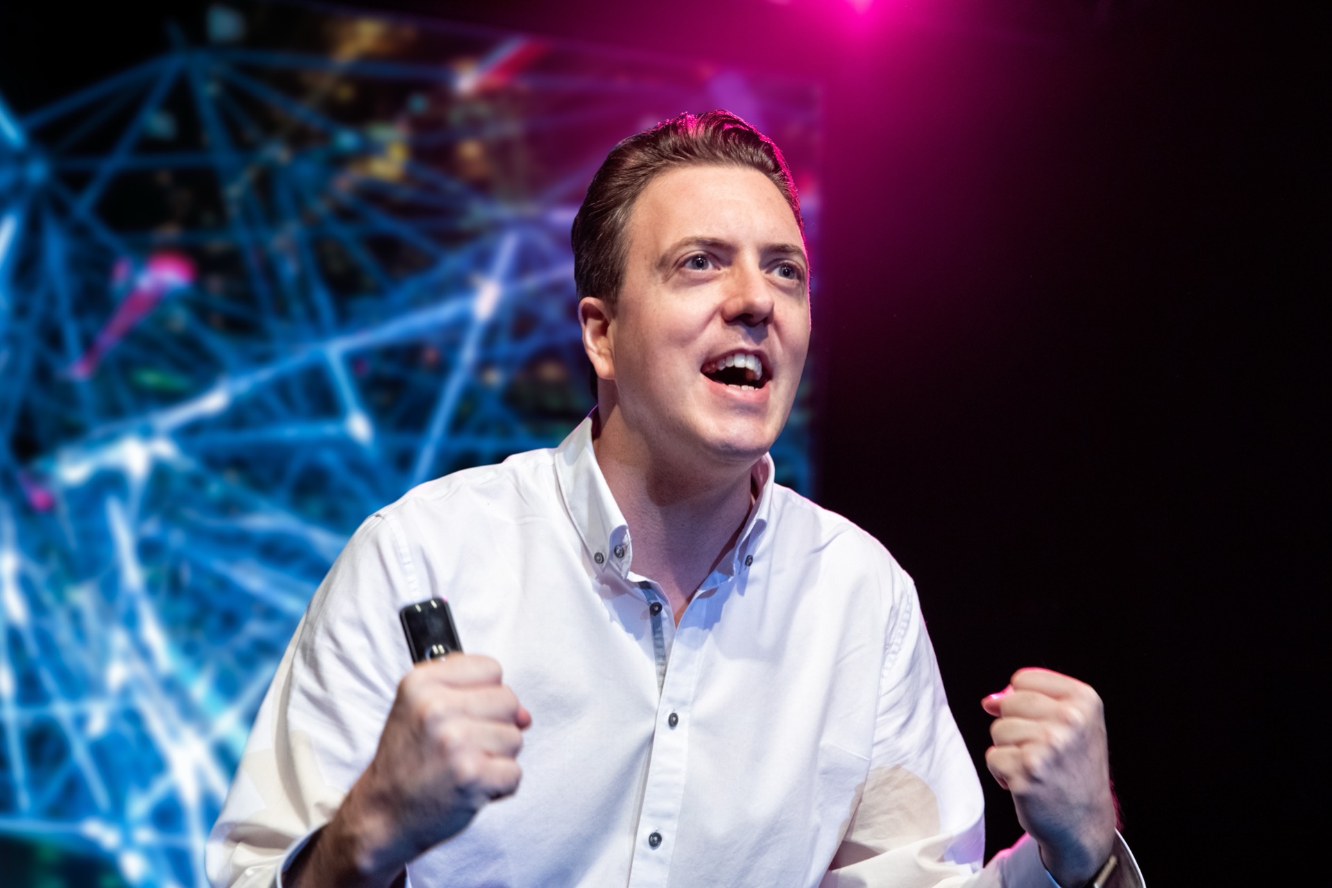 Roman Weishäupl in Nahaufnahme bei einer Keynote, hinter ihm ein leuchtendes Netzwerk-Visual