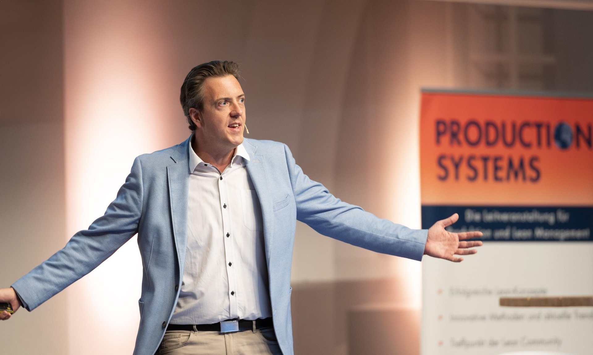 Roman Weishäupl mit ausgebreiteten Armen bei seiner Keynote auf der Production Systems von Management Circle in Stuttgart