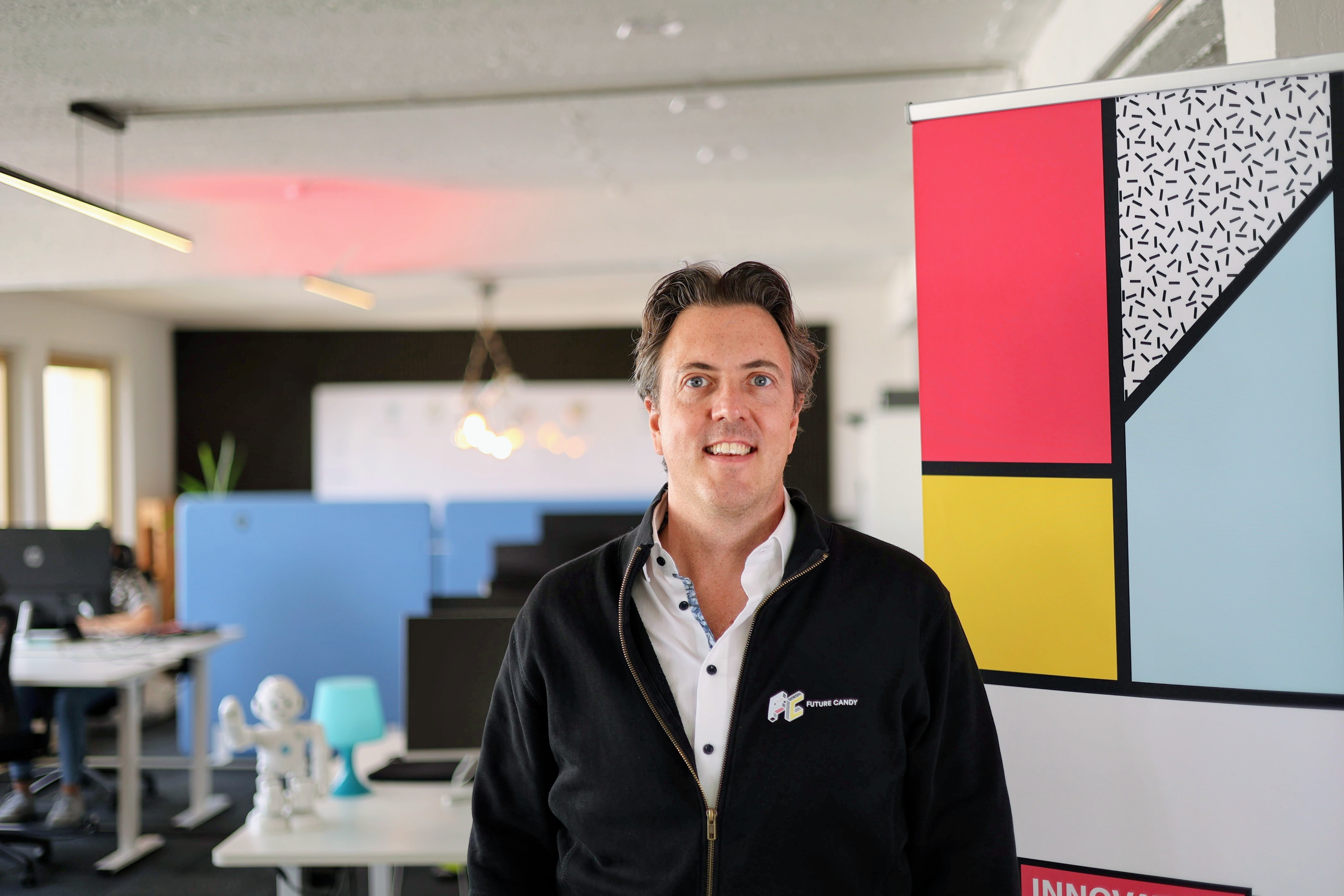 Roman Weishäupl im FUTURE CANDY Büro in Hamburg, lächelnd vor dem bunten FUTURE CANDY Roll-up